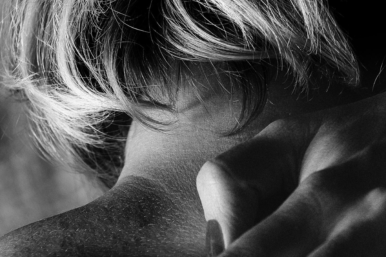 Black and white close-up of a short haircut at the nape of the neck, a hand resting on the shoulder